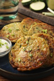 Delicious zucchini fritters with sour cream served on table, closeup