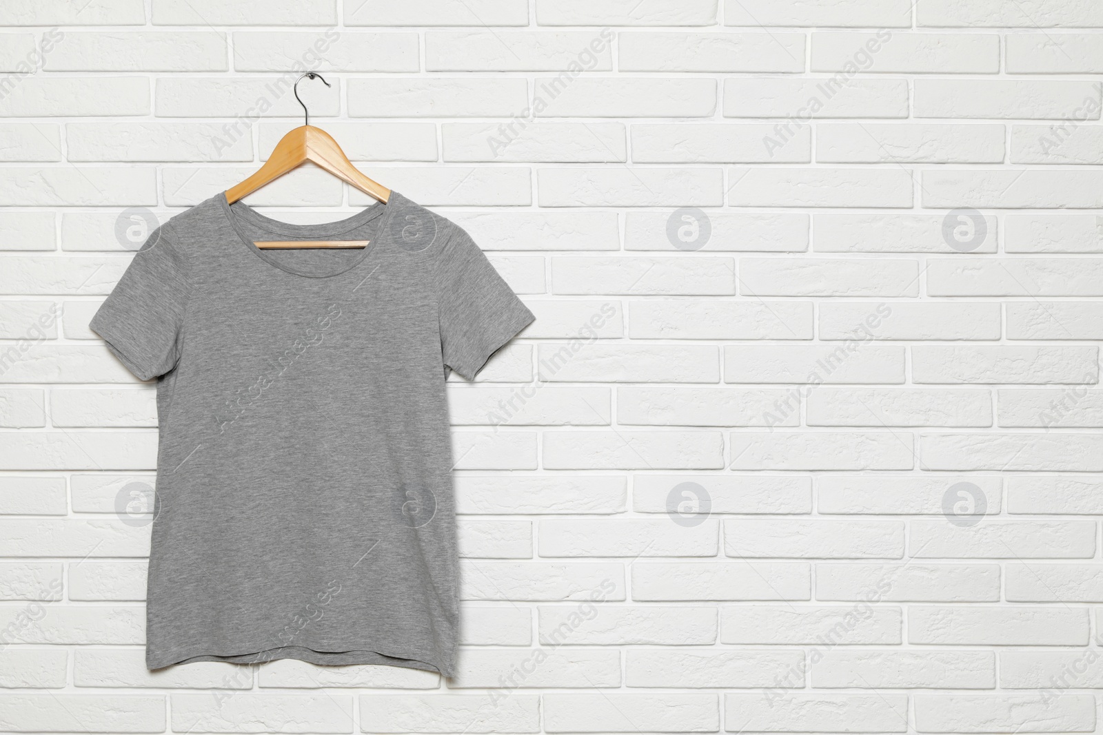 Photo of Hanger with blank t-shirt on white brick wall. Mock up for design