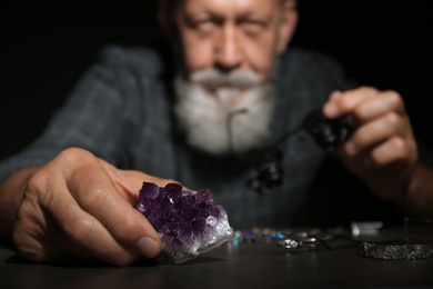 Photo of Male jeweler examining amethyst stone in workshop, closeup view