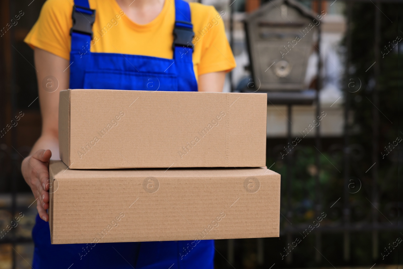 Photo of Courier in uniform with parcels near private house outdoors, closeup