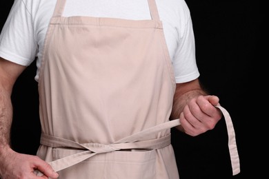 Man wearing kitchen apron on black background, closeup. Mockup for design