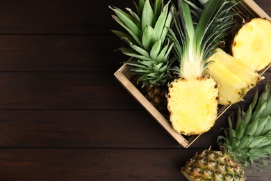 Photo of Tasty cut pineapples in crate on wooden table, flat lay. Space for text