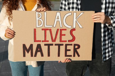 Young man and African American woman holding sign with phrase Black Lives Matter outdoors, closeup. Racism concept