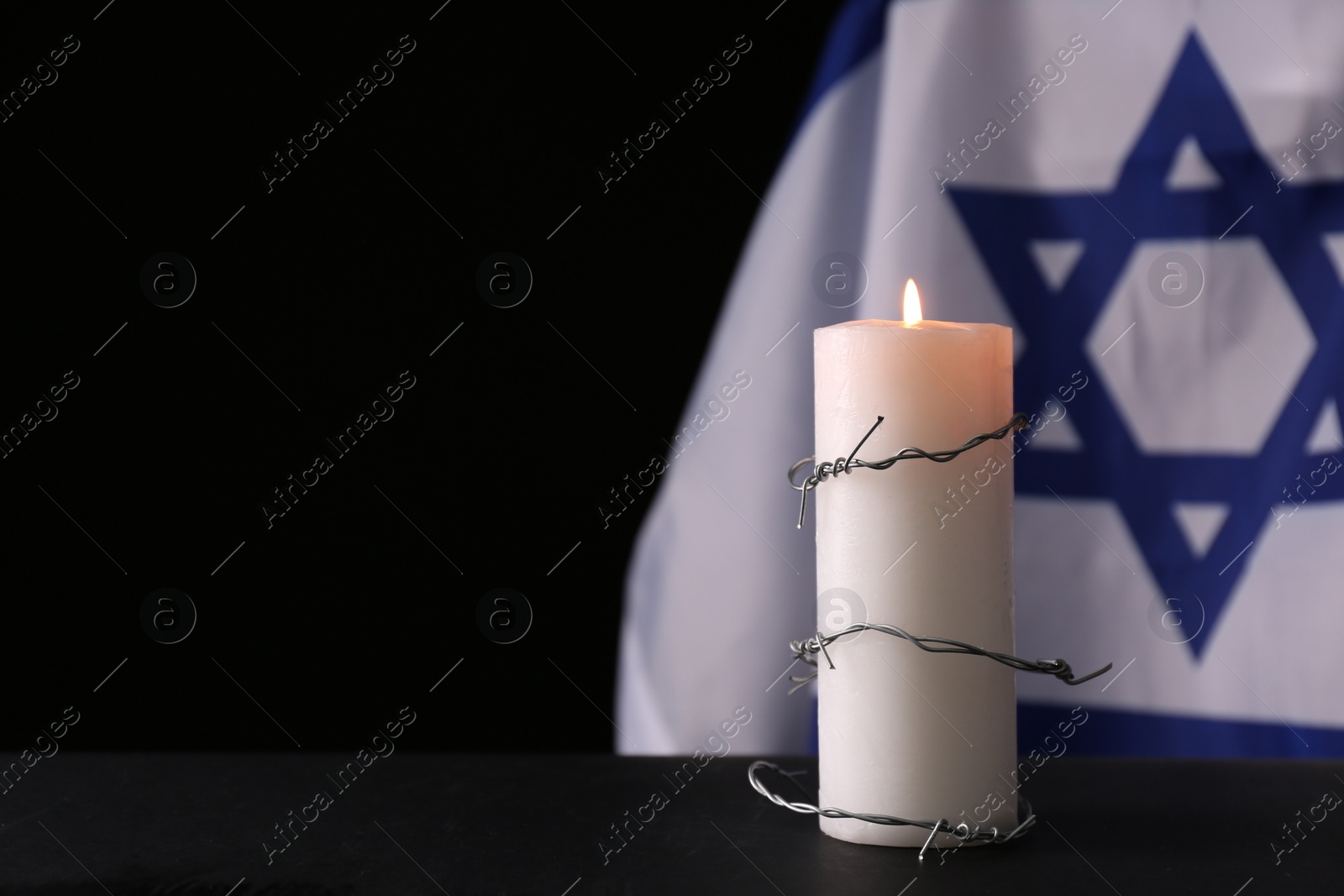 Photo of Barbed wire and burning candle on black background, space for text. Holocaust memory day