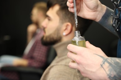 Hairdresser holding bottle of beard oil in barbershop, closeup with space for text. Professional shaving service