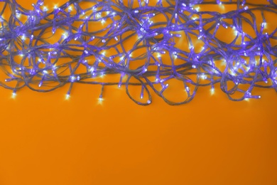 Photo of Glowing Christmas lights on yellow background, top view. Space for text