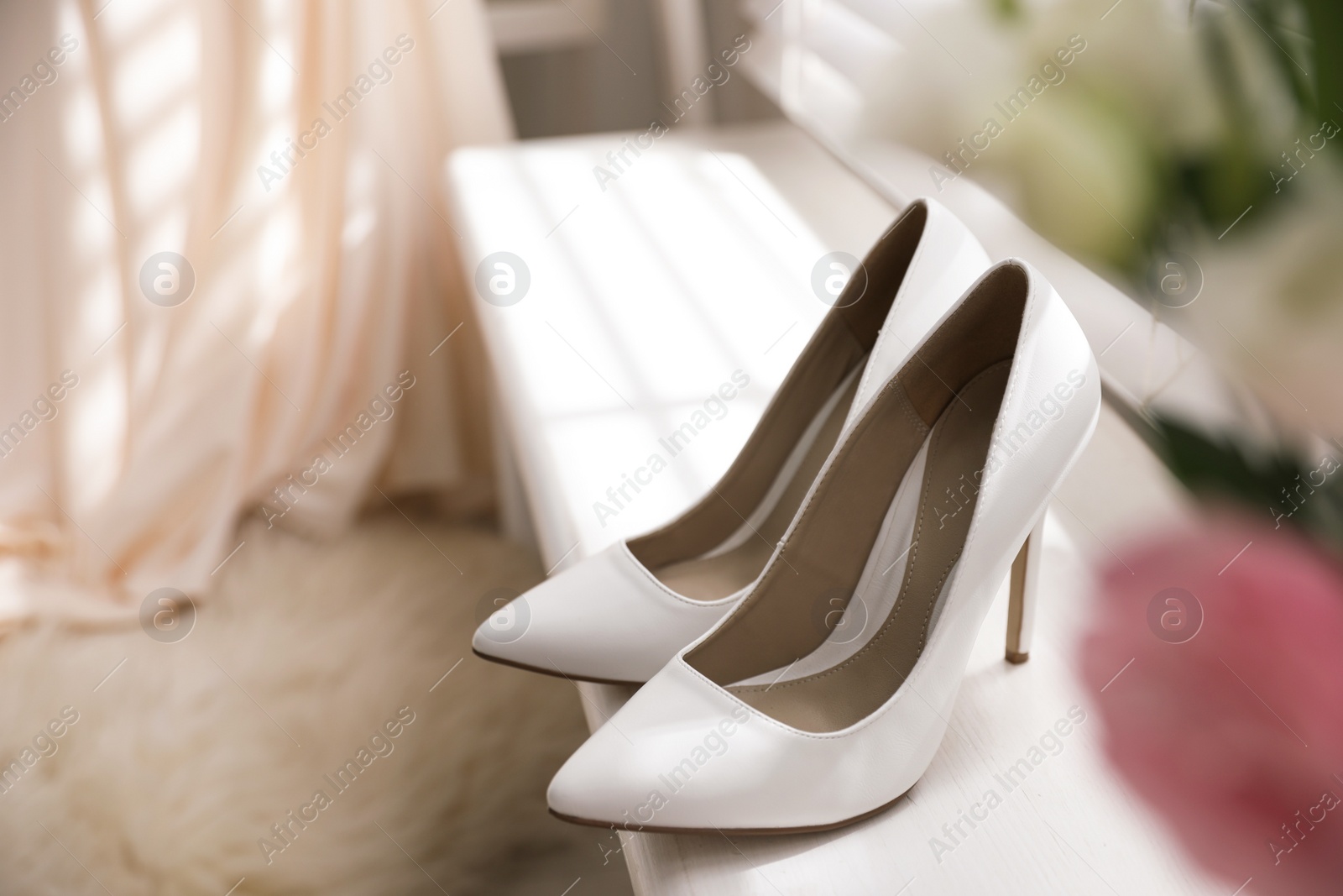 Photo of Pair of white high heel shoes and blurred wedding dress on background, space for text