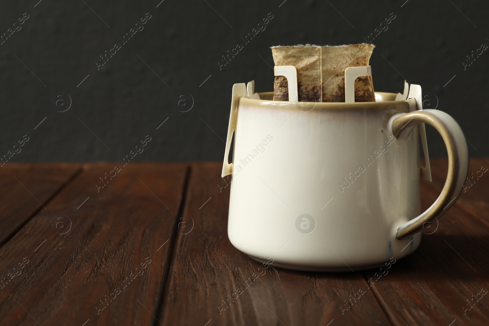 Photo of Cup with drip coffee bag on brown wooden table, closeup. Space for text