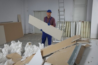 Construction worker carrying used drywall in room prepared for renovation