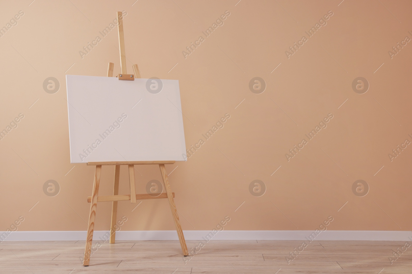 Photo of Wooden easel with blank canvas near beige wall indoors. Space for text