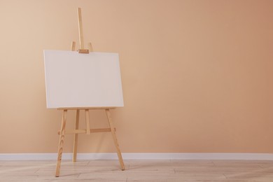 Photo of Wooden easel with blank canvas near beige wall indoors. Space for text