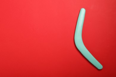 Photo of Turquoise wooden boomerang on red background, top view. Space for text