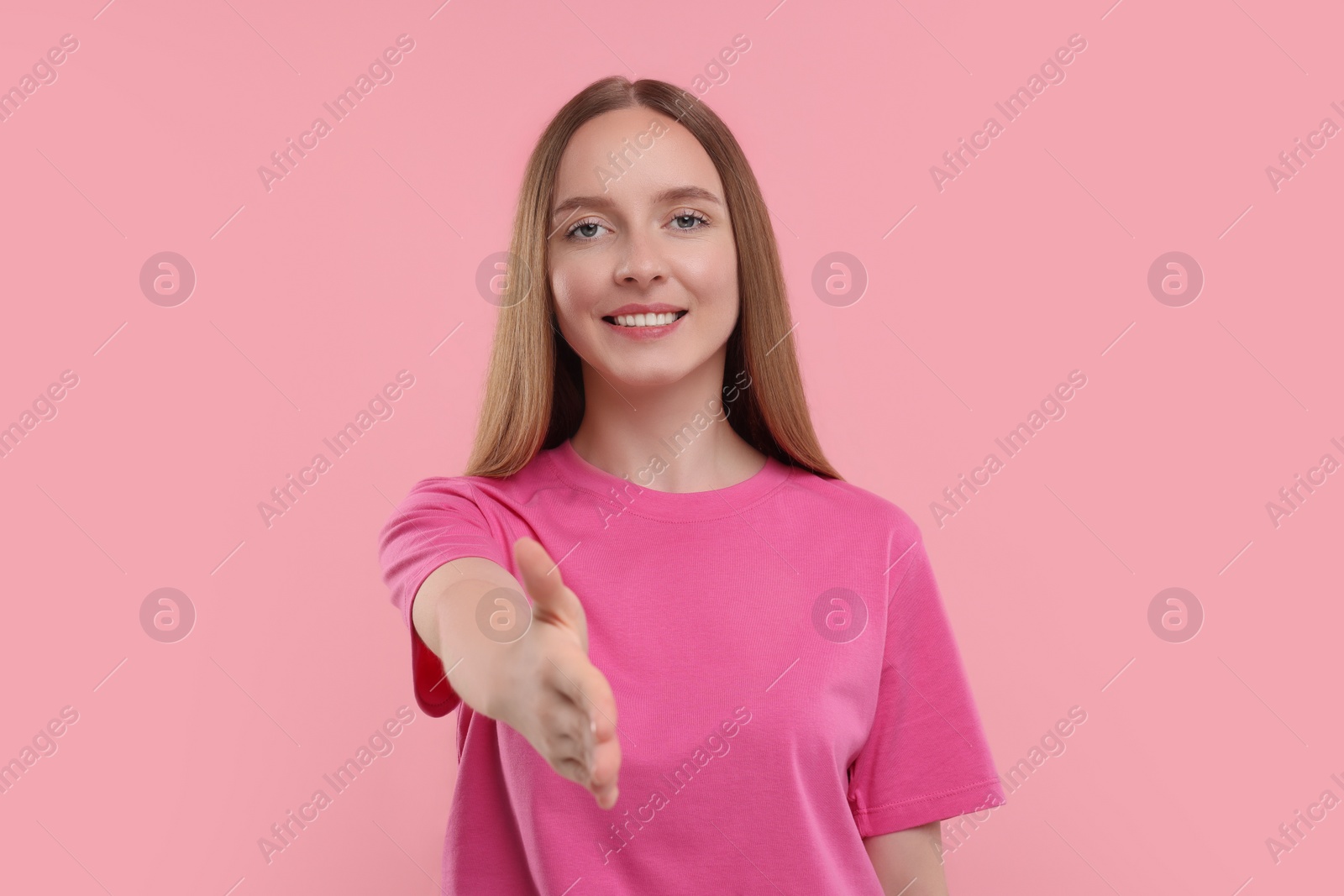 Photo of Happy young woman welcoming and offering handshake on pink background