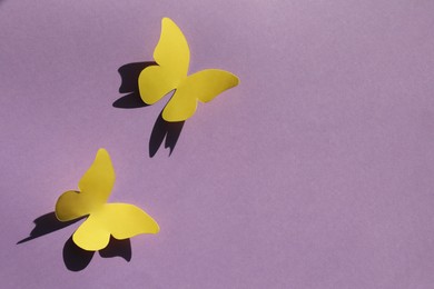 Yellow paper butterflies on violet background, top view. Space for text