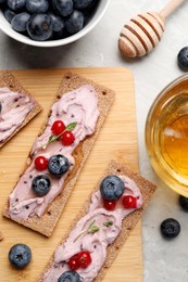 Photo of Tasty cracker sandwiches with cream cheese, blueberries, red currants, thyme and honey on grey marble table, flat lay