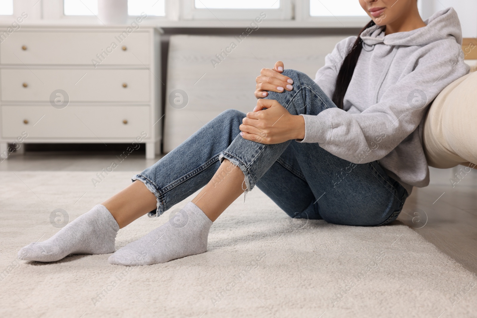 Photo of Woman suffering from knee pain on floor at home, closeup