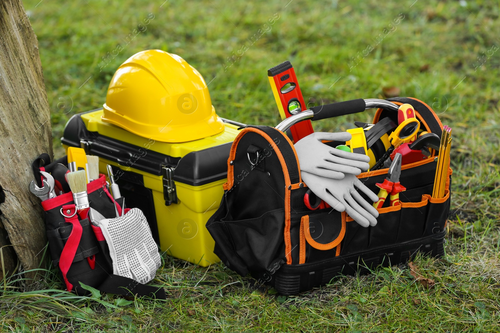 Photo of Bag, belt and box with different tools for repair on grass near tree outdoors