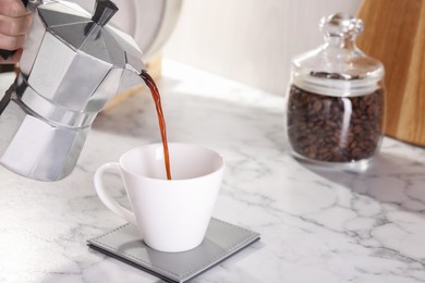 Woman pouring aromatic coffee from moka pot into cup at white marble table, closeup