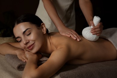 Photo of Young woman receiving herbal bag massage in spa salon