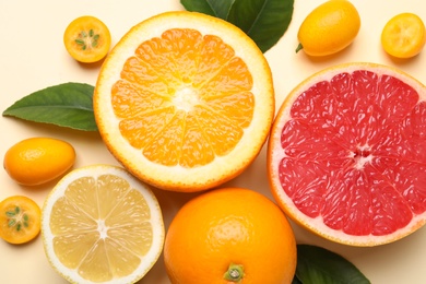 Photo of Fresh juicy citrus fruits with green leaves on beige background, flat lay