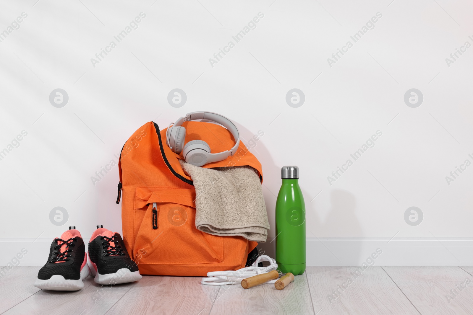 Photo of Backpack and sports equipment on floor near white wall. Space for text