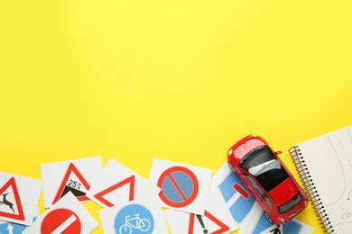 Photo of Many different road sign cards, notebook and toy car on yellow background, flat lay with space for text. Driving school