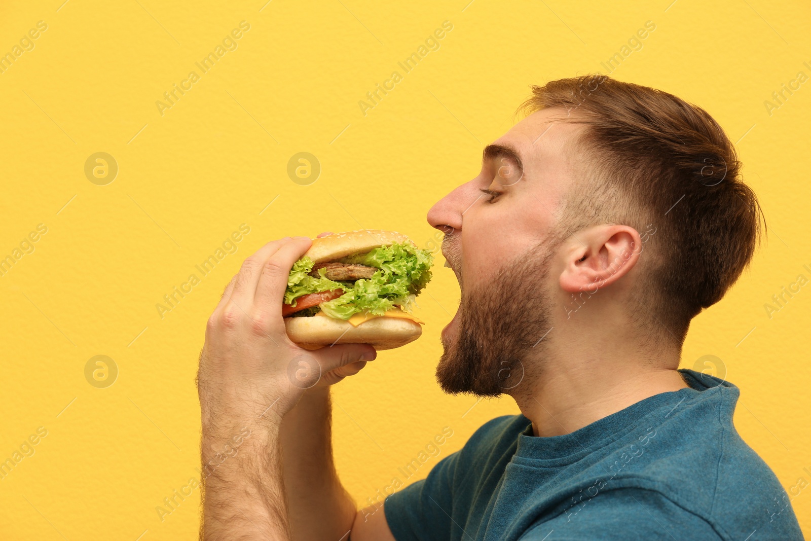 Photo of Young man eating tasty burger on color background. Space for text