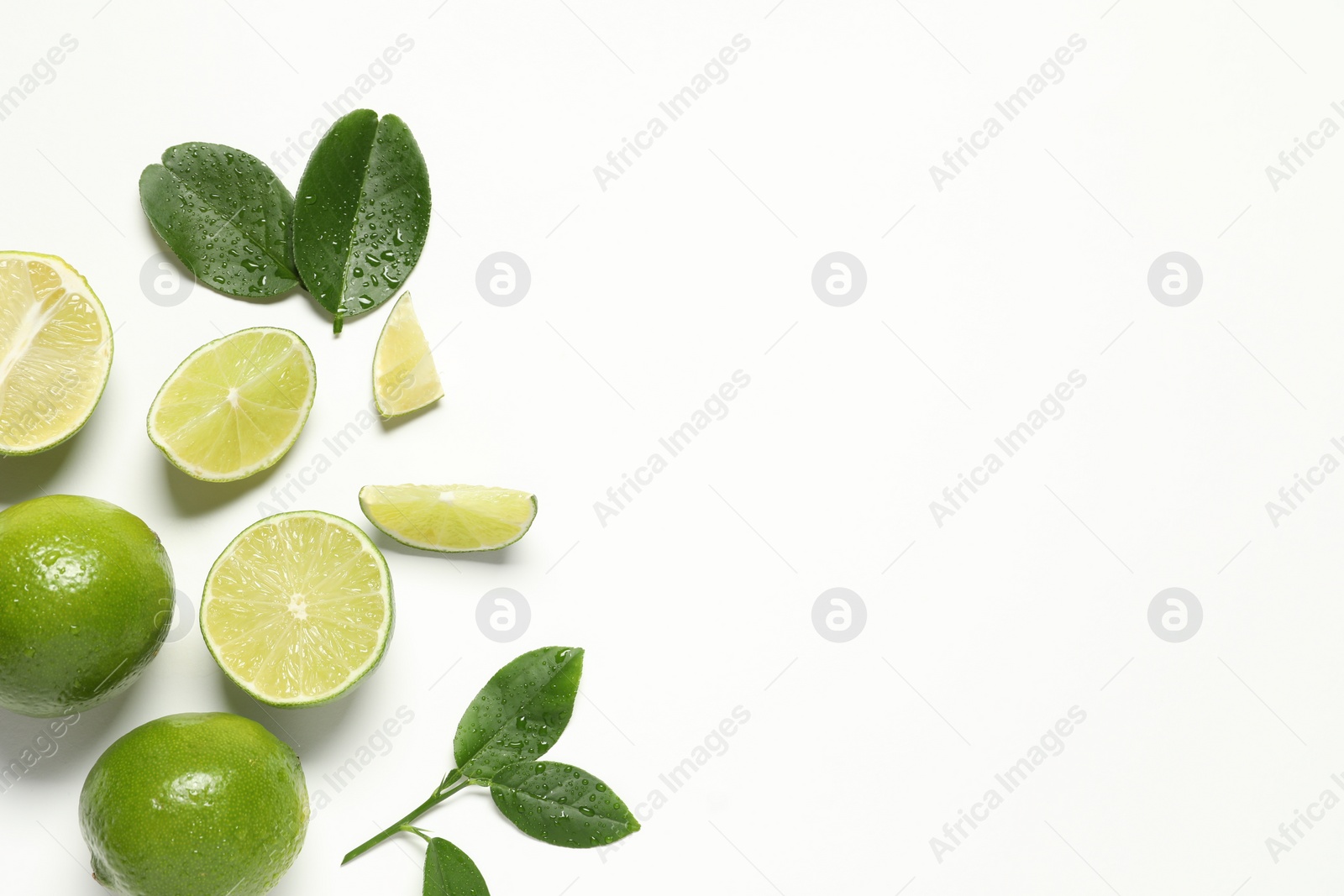 Photo of Whole and cut fresh ripe limes with green leaves on white background, flat lay