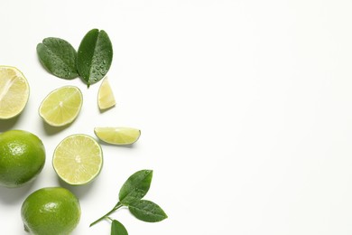 Photo of Whole and cut fresh ripe limes with green leaves on white background, flat lay