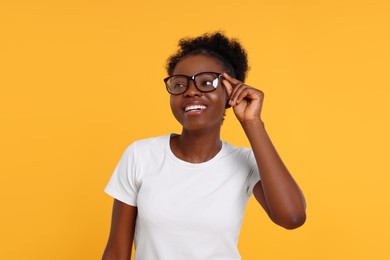 Portrait of happy young woman in eyeglasses on orange background