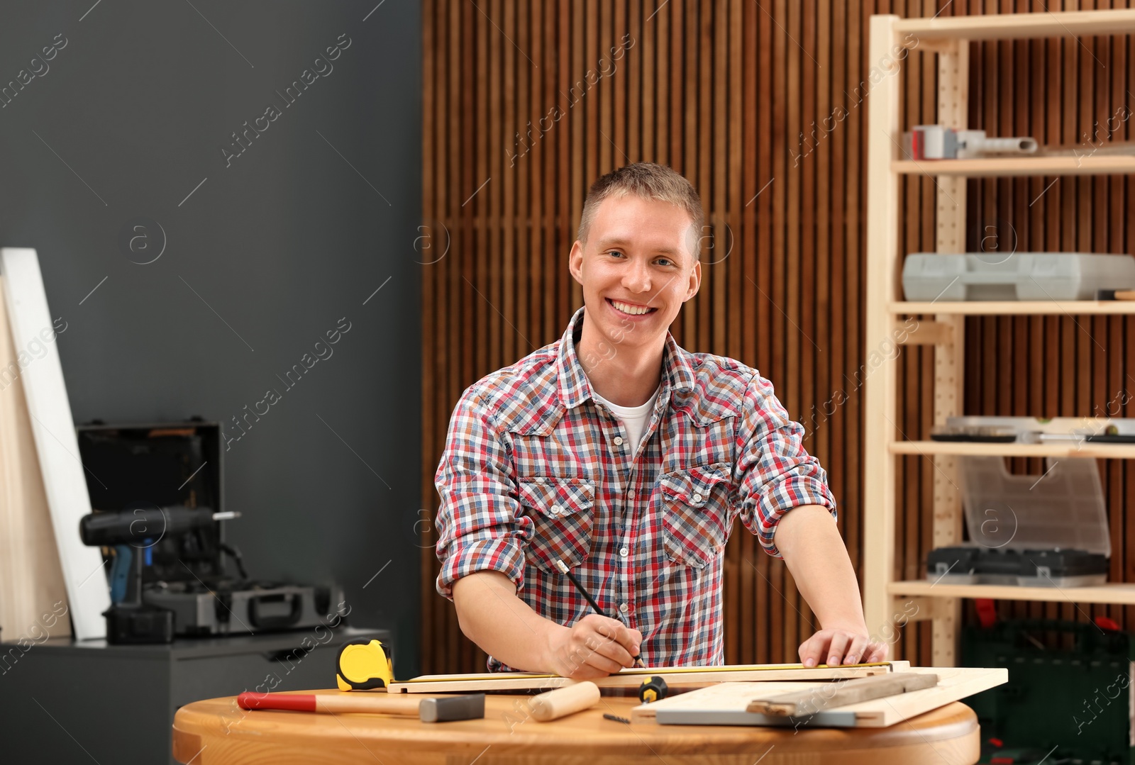 Photo of Handsome young working man making marks on timber at table indoors. Home repair