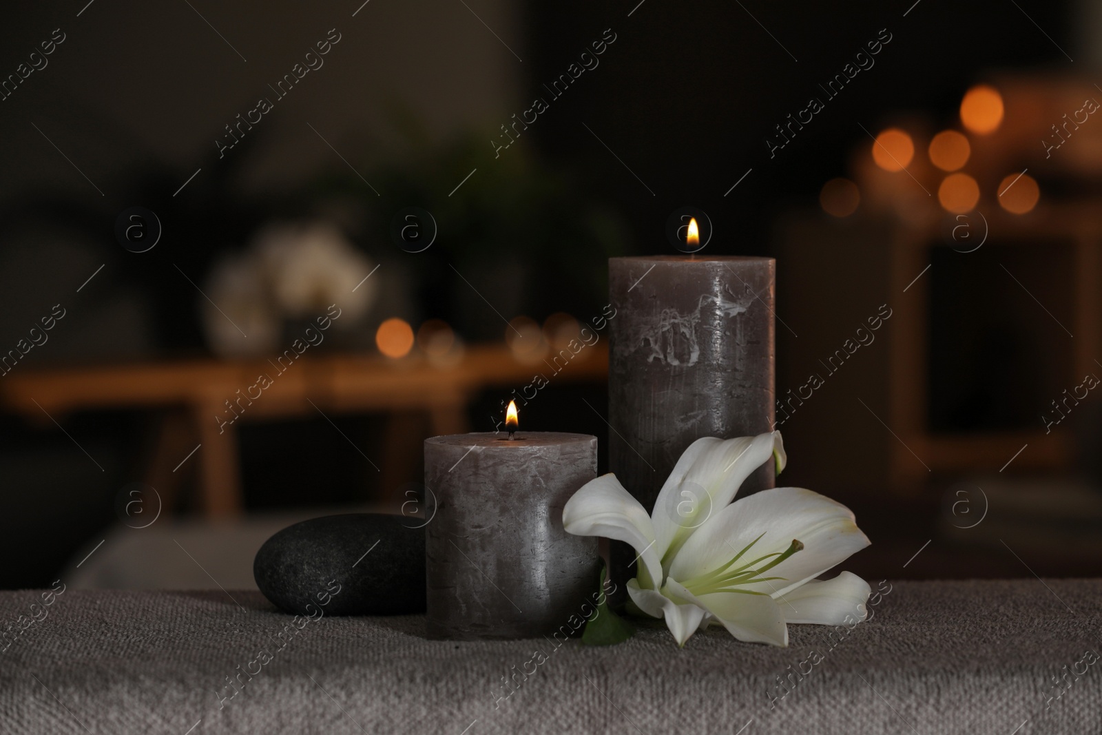 Photo of Spa composition with burning candles, lily flower and stone on massage table in wellness center