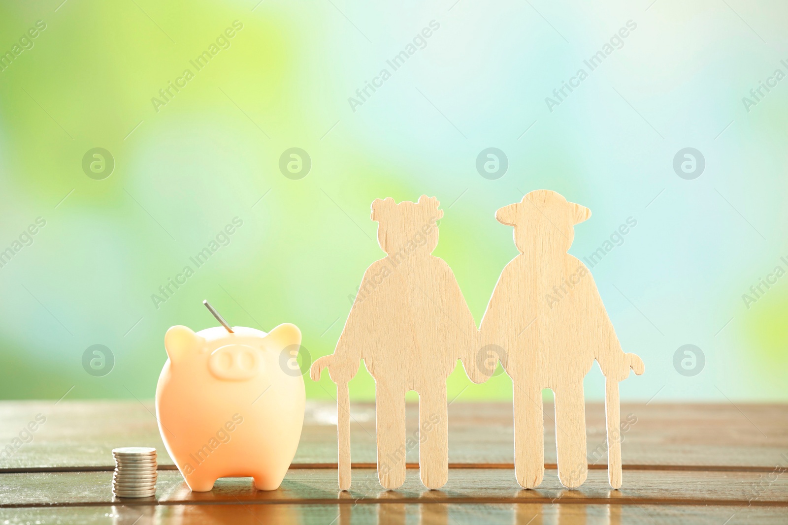 Photo of Pension savings. Figure of senior couple, piggy bank and stacked coins on wooden table against blurred background