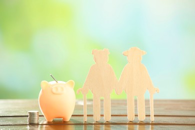 Pension savings. Figure of senior couple, piggy bank and stacked coins on wooden table against blurred background