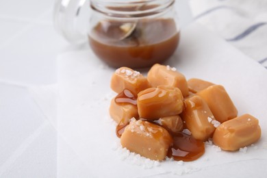 Yummy caramel candies and sea salt on white table. Space for text