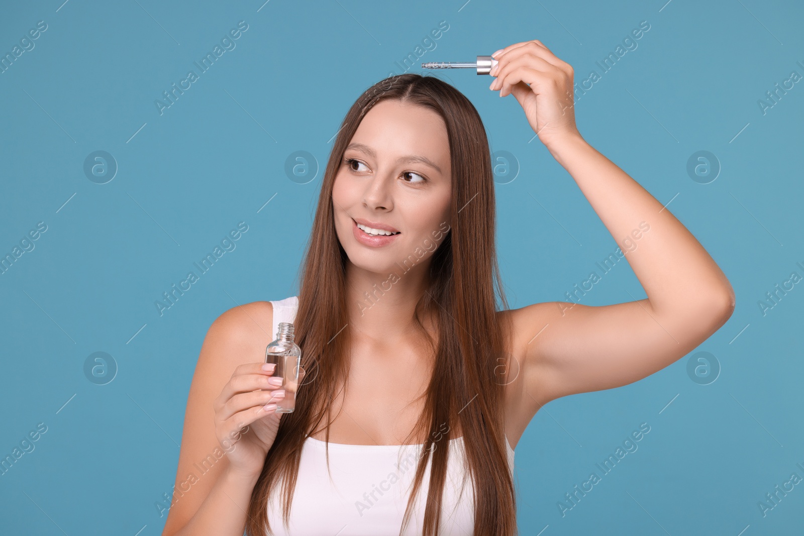 Photo of Beautiful woman applying serum onto hair on light blue background