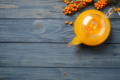 Photo of Delicious sea buckthorn tea and fresh berries on blue wooden table, flat lay. Space for text