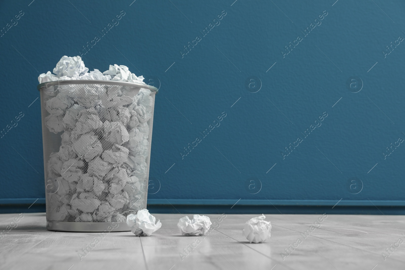 Photo of Metal bin with crumpled paper on floor against color wall. Space for text