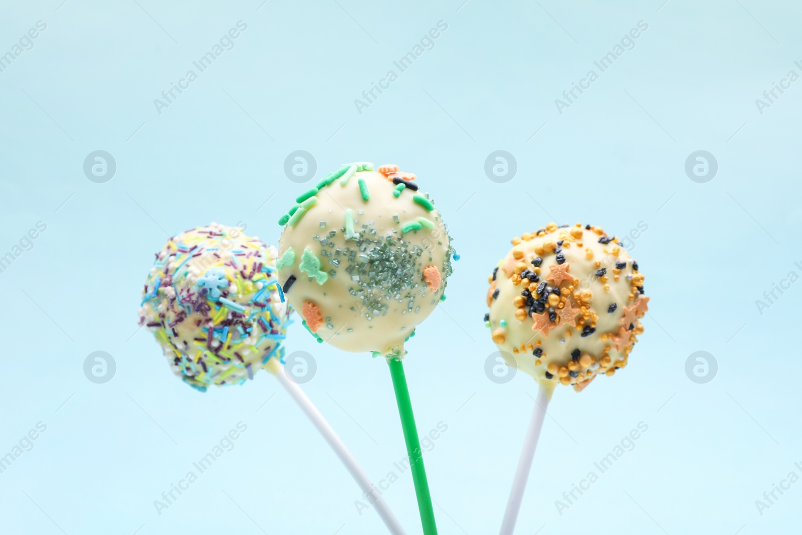 Photo of Sweet cake pops decorated with sprinkles on light blue background, closeup. Delicious confectionery