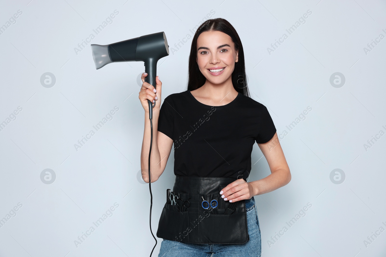 Photo of Portrait of happy hairdresser with hairdryer and professional tools on light background