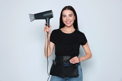 Photo of Portrait of happy hairdresser with hairdryer and professional tools on light background