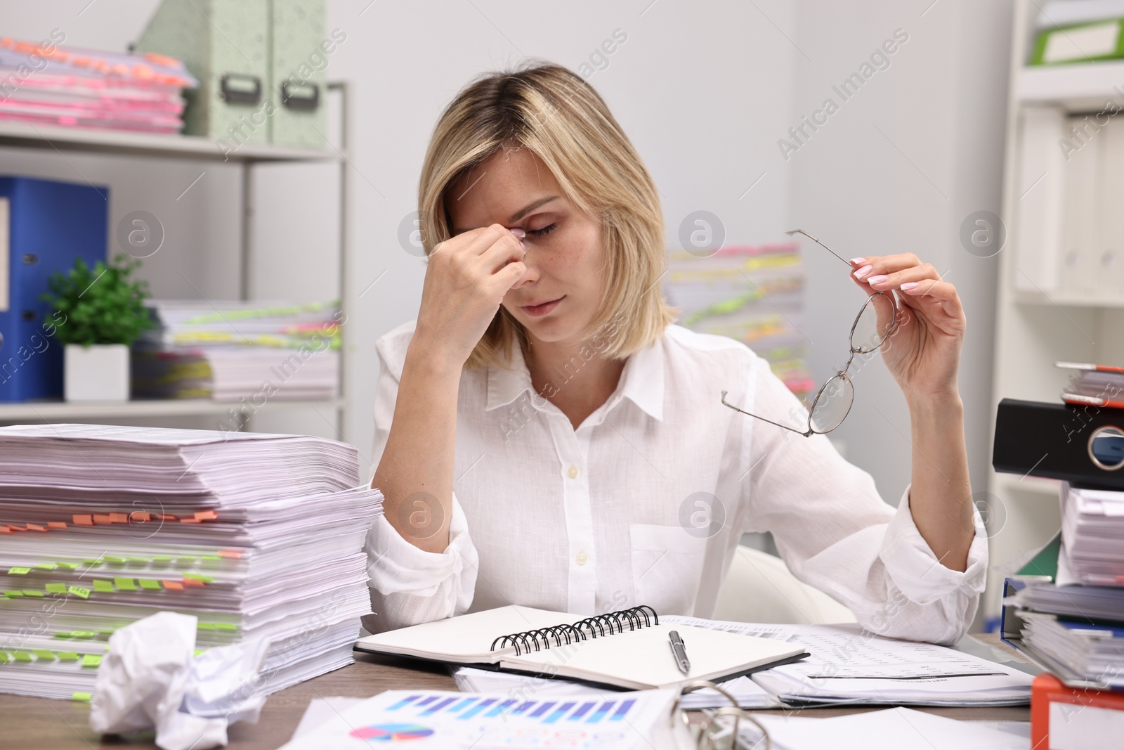 Photo of Overwhelmed woman surrounded by documents at workplace in office