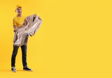 Dry-cleaning delivery. Happy courier holding coat in plastic bag on orange background, space for text