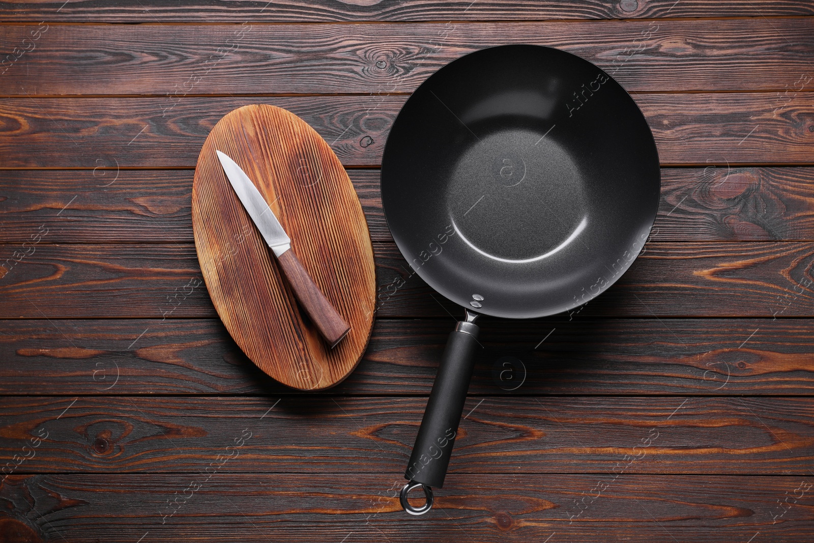 Photo of Empty iron wok, knife and cutting board on wooden table, flat lay