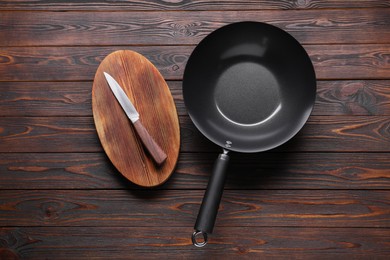 Empty iron wok, knife and cutting board on wooden table, flat lay