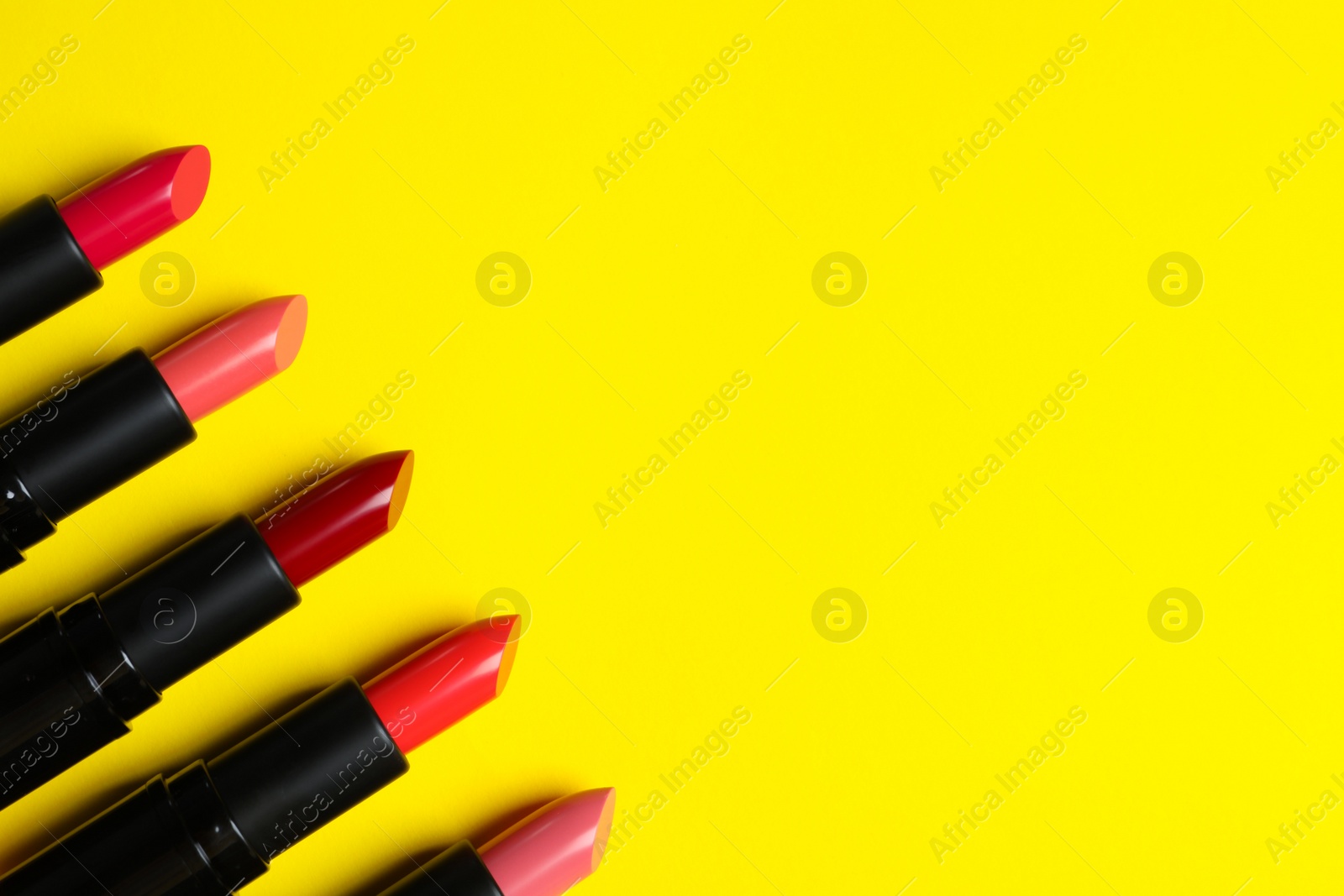 Photo of Many bright lipsticks on yellow background, flat lay. Space for text