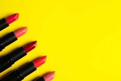 Many bright lipsticks on yellow background, flat lay. Space for text
