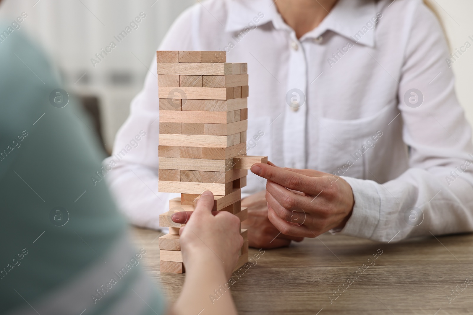 Photo of People playing Jenga tower at wooden table indoors, closeup