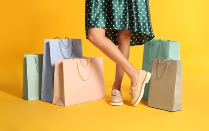 Photo of Young woman with paper shopping bags on yellow background, closeup