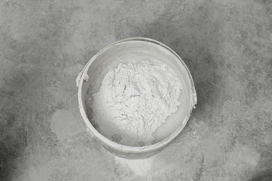 Photo of Bucket with powdered plaster and liquid on concrete floor, top view